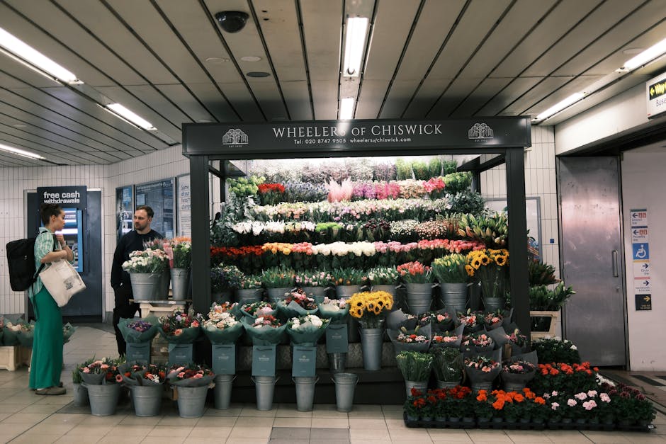 A vibrant flower display at Wheeler of Chiswick in a busy underground station, featuring an arrangement of various fresh flowers including yellow sunflowers, pink roses, white lilies, purple tulips, a