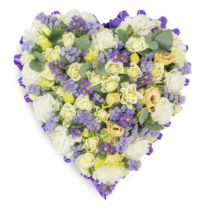 A meticulously arranged heart-shaped floral tribute, photographed on a clean white studio surface so every detail is visible; the perimeter is neatly finished with a continuous purple satin ribbon that creates an elegant frame and a subtle sheen. Inside the heart, a soft, harmonious palette of white, cream and pale yellow blooms is densely packed to create a plush, sculpted form: numerous cream and pale yellow roses-some as tight buds, others just beginning to unfurl with faint touches of green-sit shoulder to shoulder with generous clusters of ruffled white carnations, lending weight and classic sympathy notes to the composition. Interspersed through this pale foundation are fine sprays of lavender statice and small, vivid purple aster-type flowers with bright yellow centers, which punctuate the design with lively colour and delicate texture. Scattered blue-green eucalyptus leaves introduce a modern silvery tone and rounded shapes that ease the visual density, suggesting a cool, faint fragrance rising from the arrangement. The lighting is soft and even, accentuating petal surfaces and the ribbon's lustre without dramatic shadows, conveying a quiet, respectful mood. Crafted with funeral and memorial purposes in mind, this heart would be a fitting tribute at wakes or graveside services throughout Cheam, North Cheam or Stonecot Hill; prepared by Cheam Flowers, it embodies consolation, enduring affection and thoughtful craftsmanship, offering a serene and dignified way to express sympathy and honour a cherished memory.