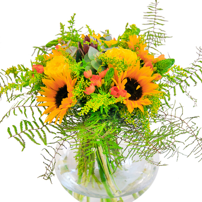 In Cheam, where gardens flourish and heritage blends with modern living, this sun-filled arrangement is a nod to both tradition and contemporary taste. Bold sunflowers, their dark centres ringed with luminous yellow-orange petals, appear to collect and reflect light as if echoing a summer afternoon by the gardens of Nonsuch Mansion. Nestling alongside, yellow garden roses spiral open with astonishing fullness, their overlapping petals inviting a closer look and a breath of their delicate scent. The bouquet's signature pop comes from numerous bright red Hypericum berries, playing against the golden yellow with bursts of cheerful, almost celebratory colour. Soft, feathery green fronds spill naturally over the edges, mimicking the gentle sway of tree branches in Mayfield Lavender fields not far from Cheam. Airy accents of goldenrod or solidago introduce mini sprays of yellow while slender, upright greenery and traces of eucalyptus contribute dimension and freshness. The bouquet rests in a clear, rounded glass vase, each stem elegantly displayed and the water below imparting a sense of purity. This expertly assembled bouquet is an ideal decorative piece for a family celebration, a congratulatory wish, or simply a heartfelt gesture to brighten up a living space in the heart of Cheam.